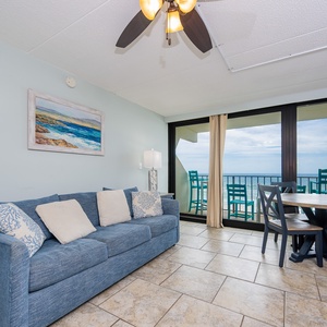 The living area features a comfortable couch and a dining table, with stunning beachfront views just beyond the glass doors