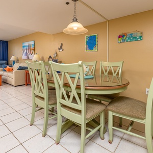 Dining area with a round table, colorful decor, and a view of the beach off the balcony through large windows