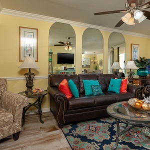 The living room features a dark leather sofa with queen sleeper, a glass coffee table, and decorative accents