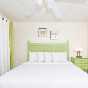 The guest bedroom features a light green headboard, queen bed, soft white linens, and vibrant curtains