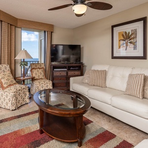 Cozy living area features a white leather sofa with queen sleeper, two patterned chairs, and a view of the beach