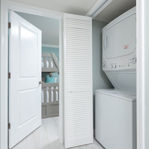A laundry area features a stacked washer and dryer, with a glimpse of a cozy bunk bed room beyond the open door
