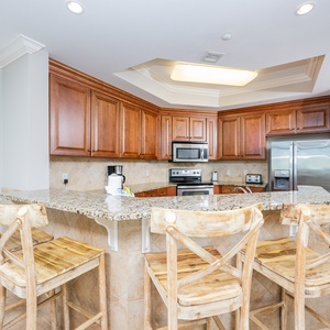 This kitchen features wooden cabinetry, granite countertops, stainless appliances, and a cozy breakfast bar for casual dining