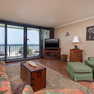 This living area features vibrant floral decor, a TV, and a stunning beachfront view through large sliding glass doors