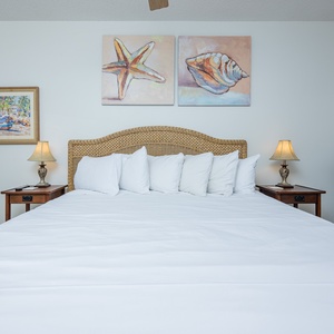 Spacious guest bedroom featuring a king-size bed, coastal artwork, and warm lighting for a restful retreat