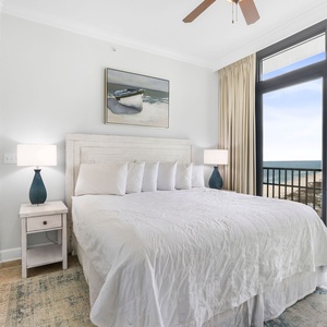 This bedroom features a serene white palette, a cozy king bed, and large windows offering a stunning beachfront view