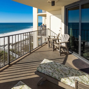 The balcony features comfortable seating with a vibrant floral pattern and offers a panoramic view of the tranquil beach