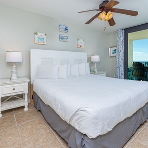 Master suite bedroom featuring a king bed, coastal art, and sliding glass doors leading to a balcony with beach views