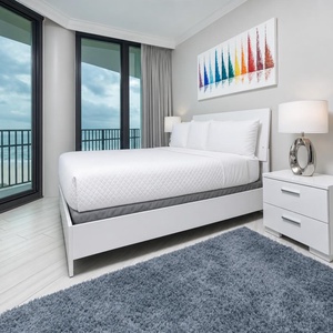 Relax in this guest bedroom featuring a plush queen bed, stylish decor, and a balcony offering beach views