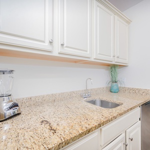 Wet bar with granite countertops, a modern sink, and a glimpse of the stunning coastal view beyond