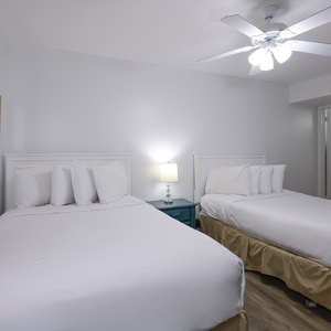 Guest bedroom features two double beds with white linens, a nightstand, and a ceiling fan, creating a relaxing atmosphere