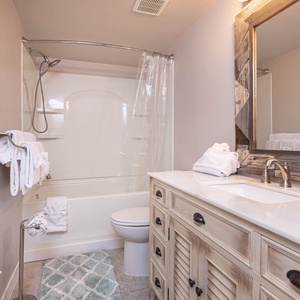 The guest bathroom features a stylish vanity, rustic mirror, fresh towels, and a clean tub-shower combo for a relaxing stay