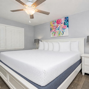 The master bedroom features a large, inviting bed with crisp white linens, stylish decor, and a colorful floral painting