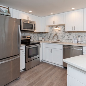 The modern kitchen features sleek white cabinetry, a stylish backsplash, and a full suite of stainless appliances
