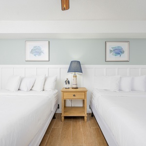 Enjoy restful nights in this inviting guest room featuring two queen beds and coastal artwork