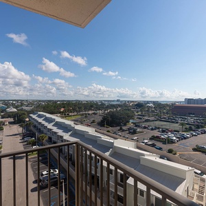 Balcony from master showcases vibrant surroundings with lush greenery, parking areas, and view of the bay in the distance