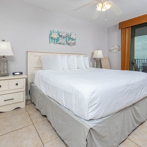 Master bedroom featuring a king bed, a bedside lamp, and a balcony view of the beach beyond large sliding doors