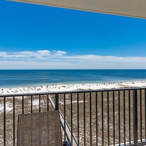 Balcony view overlooking the beach with white sand, colorful umbrellas, and a serene gulf stretching to the horizon