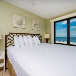 This bedroom features a large bed with plush pillows and a stunning beachfront view through the expansive window