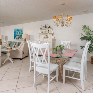Dining area features a glass-top table with white chairs, surrounded by a cozy living space and tropical decor