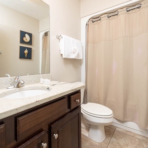 This bathroom features a stylish vanity with a granite countertop, a shower curtain in soft beige, and coastal-themed artwork