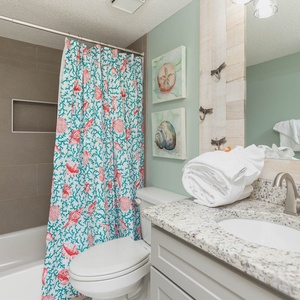 The guest bathroom features a colorful shell-patterned shower curtain, a granite countertop, and neatly arranged towels