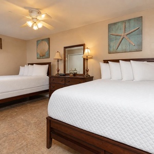 This guest bedroom features two double beds, coastal-themed artwork, and warm lighting for a relaxing retreat