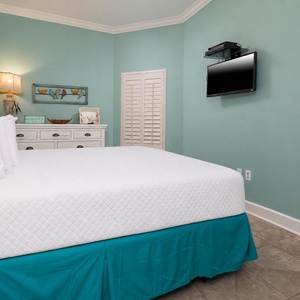 This bedroom features a calming teal wall, a cozy king quilted bed, and a wall-mounted TV for your entertainment