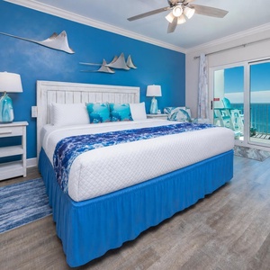 The master bedroom features a king-size bed with ocean-themed decor and a stunning beachfront view from the private balcony