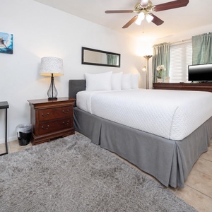 This cozy bedroom features a plush bed, a TV for entertainment, and soft, natural light from the window