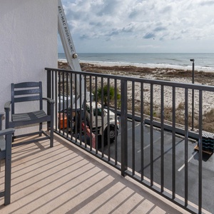 The balcony features two comfortable chairs and a view of the serene beach, perfect for relaxation and enjoying the scenery