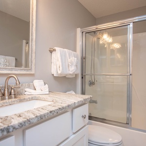 Stylish guest bathroom featuring a spacious vanity with elegant fixtures, plush towels, and a glass-enclosed tub/shower