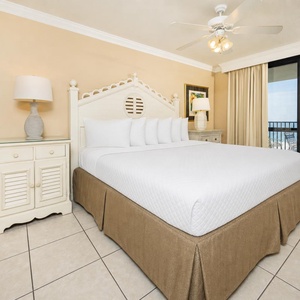 Master bedroom features a king bed, coastal-inspired furnishings, and a sliding door leading to a balcony with gulf views