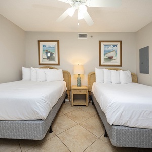 Two double beds with plush white bedding and coastal artwork create a serene atmosphere in this inviting guest bedroom