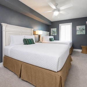 Unwind in the serene guest bedroom featuring two double beds with soft bedding, a TV, and coastal decor