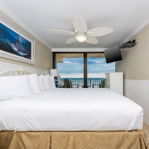 This bedroom features a plush king bed, a mounted TV, and a stunning beachfront view through large sliding glass doors