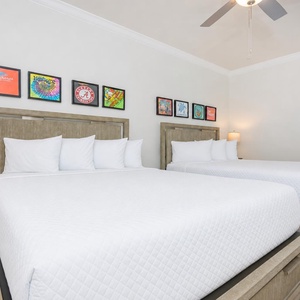 Rest in this guest bedroom featuring two queen beds, stylish decor, and vibrant artwork on the walls