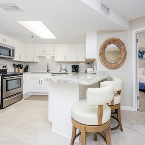 White cabinetry complements this modern kitchen with a marbled countertop and tasteful seating at the breakfast bar