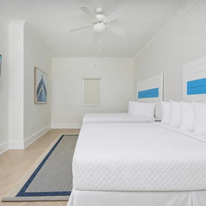Relax in this guest bedroom featuring two beds with blue accents, a large TV, and coastal decor