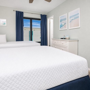 This guest bedroom features two comfortable beds, light blue accents, and a view of the beach through large windows