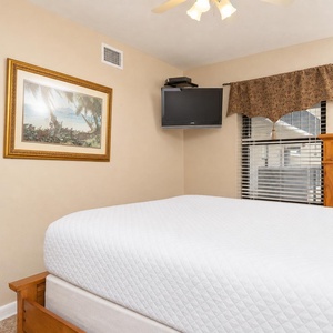 Warm-toned walls complement the wooden dresser and framed beach artwork in this cozy guest bedroom featuring a mounted TV