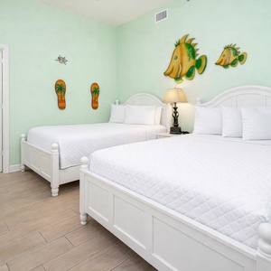 Cheerful guest room featuring two beds, a queen and a double, beach decor, and a cozy atmosphere