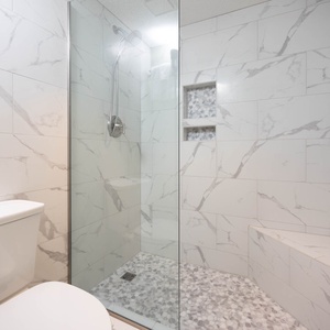 Master bathroom featuring a sleek walk-in shower with elegant marbled tiles and a stylish pebble floor