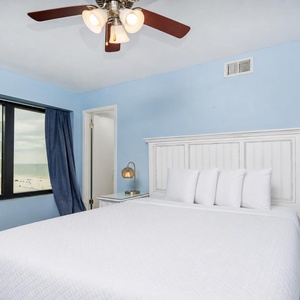 This bedroom features a comfortable bed, blue walls, and a view of the beach through large windows