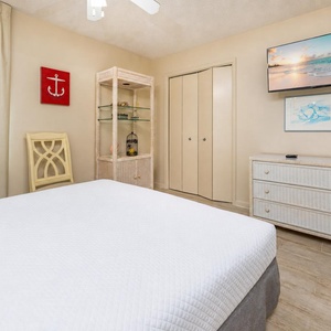 Bright guest bedroom featuring a queen bed, a TV on a dresser, and a mirror, with a closet and light-colored decor