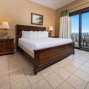 Spacious master bedroom featuring a king bed, elegant wooden furnishings, and access to a balcony with a beach front view
