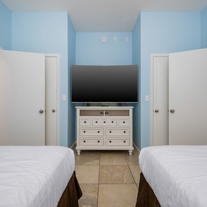 Relax in this inviting guest bedroom featuring double beds, a large TV, and a stylish dresser against soothing blue walls