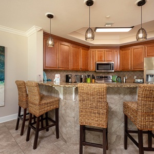 This kitchen features warm wood cabinetry, granite countertops, stainless appliances, and a cozy bar area with woven stools