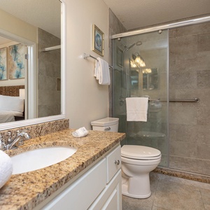 Granite countertop with a sink and plush towels complements the glass-enclosed walk-in shower in this inviting bathroom