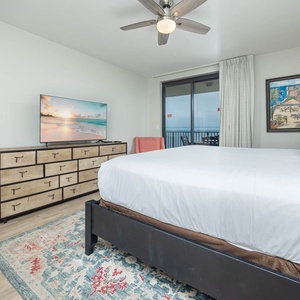 Charming master bedroom featuring a large king bed, a TV, and a chair with a beach view through sliding glass doors